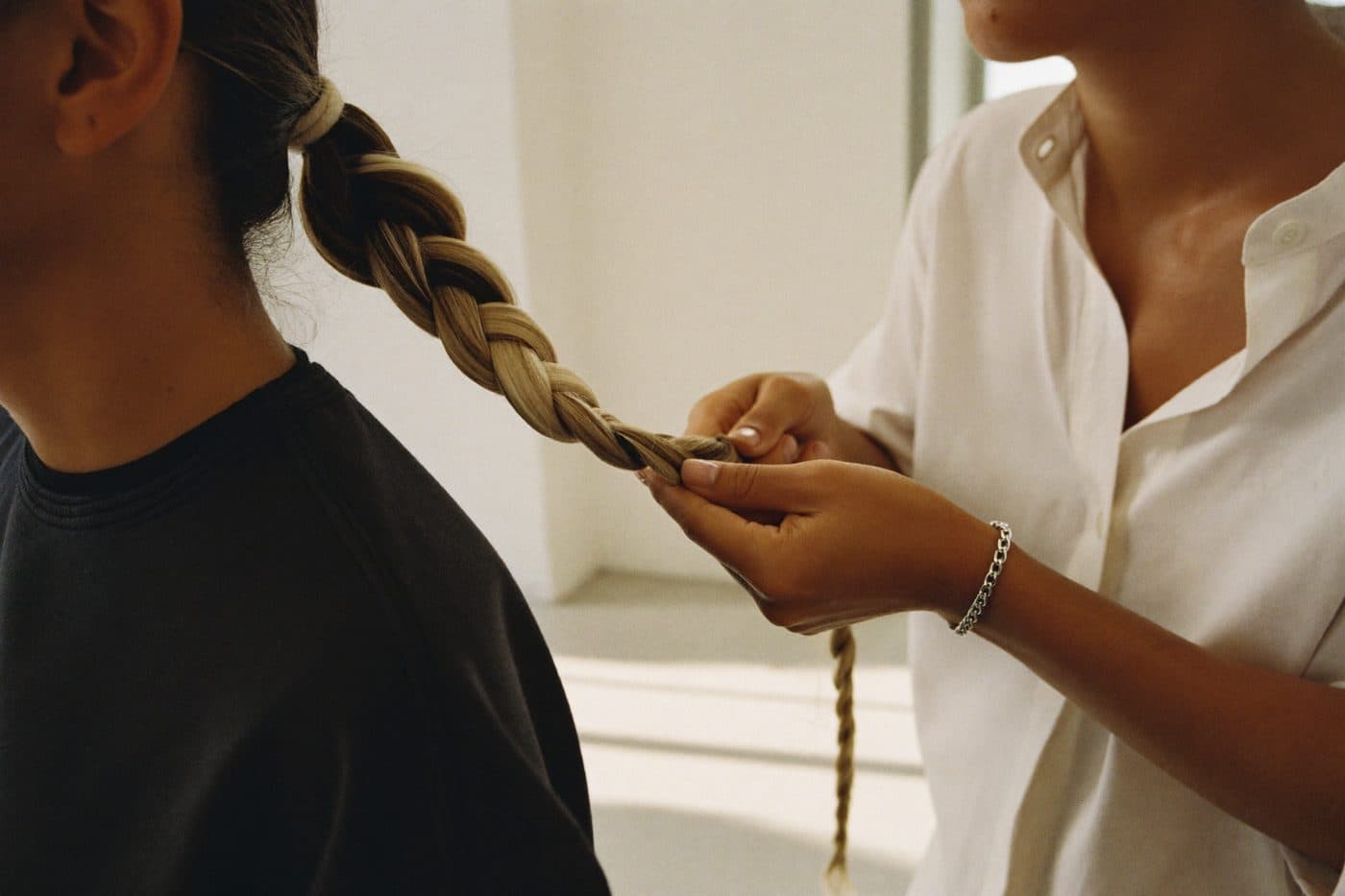 Mains d’une coiffeuse tressant une natte dans un salon lumineux
